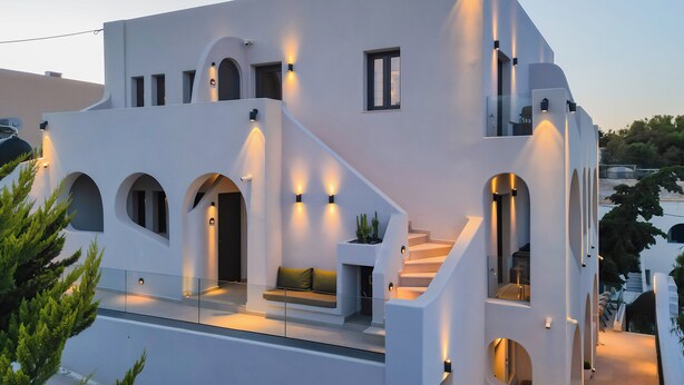 A modern white building with arched windows, a staircase, and outdoor seating. - Anemone Luxury Suites (Santorini)