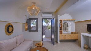 A modern living room with a sofa, a coffee table, a hanging light fixture, and a view through an open door. - Anemone Luxury Suites (Santorini)