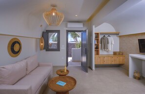 A modern living room with a sofa, a coffee table, a hanging light fixture, and a view through an open door. - Anemone Luxury Suites (Santorini)