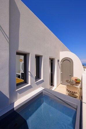 A modern pool area with a clear blue pool, a door, and a small table with a basket of fruit. - Anemone Luxury Suites (Santorini)