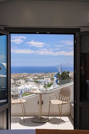 A balcony with two chairs and a table, overlooking a coastal town with buildings and the sea. - Anemone Luxury Suites (Santorini)