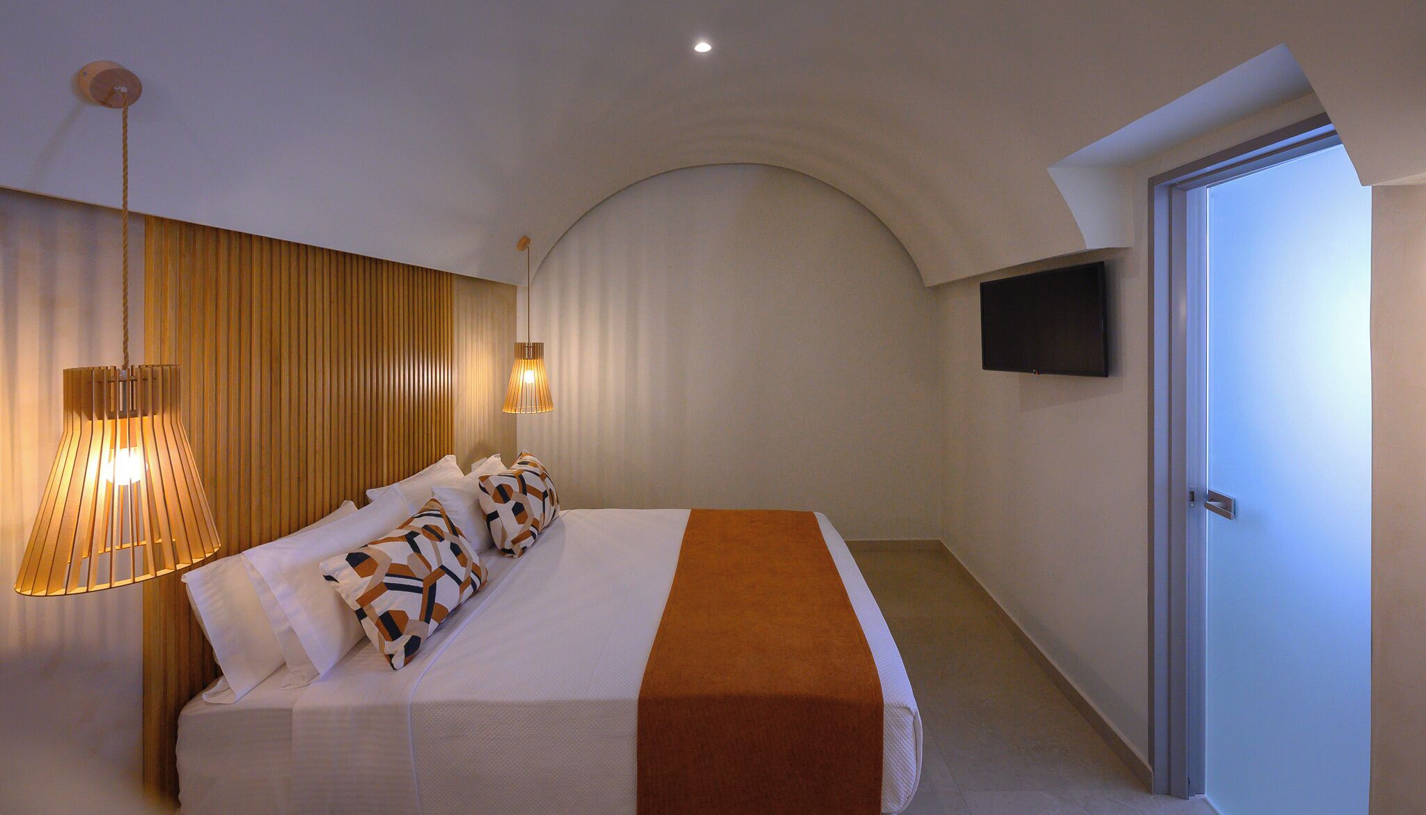 A bedroom with a bed, a wall-mounted TV, a ceiling fan, and a door.