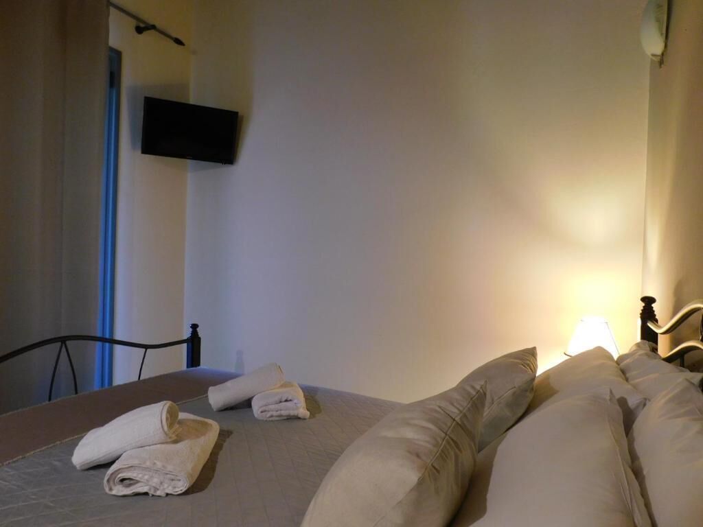 Ein Hotelzimmer mit Bett, Kissen, einem an der Wand montierten Flachbildfernseher und einem Nachttisch mit Lampe.