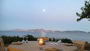 An outdoor dining table set with candles, wine glasses, and plates, overlooking a body of water with distant hills. - Vassia Holiday Home's (Ermionida)