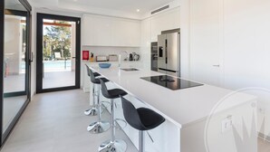 Une cuisine moderne avec des meubles blancs, un réfrigérateur en acier inoxydable et un grand îlot central doté de tabourets de bar.