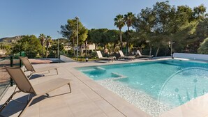 Une piscine entourée d’arbres, avec des chaises longues, sous un ciel dégagé.