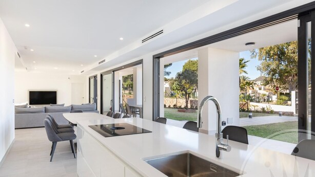 Une cuisine moderne dotée d’un grand îlot central, d’appareils électroménagers intégrés et offrant une vue sur le jardin extérieur.
