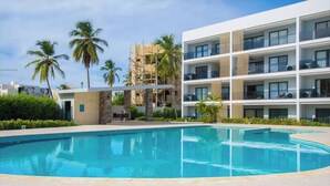 Ein modernes Hotel mit Pool, Palmen und blauem Himmel.