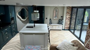 Una cucina moderna con mobili scuri, un'isola centrale e un'area pranzo con un divano marrone e poggiapiedi decorato.