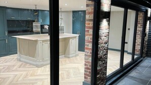 Una cucina moderna con mobili scuri, un'isola centrale e un pavimento con un motivo a spina di pesce.