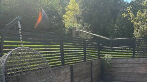 Una poltrona sospesa con cuscini, una lampada a sospensione e un recinto di legno con una pianta.