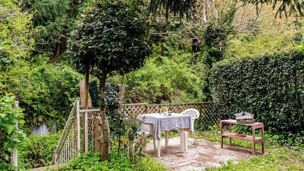A garden patio with a table and chairs, surrounded by lush greenery and a wooden fence. - Casa Laura - Nature and Art Near Florence (Rufina)