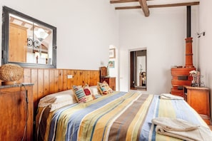 A cozy bedroom with a wooden headboard, a large bed with striped bedding, a wooden dresser, and a traditional wood-burning stove. - Casa Laura - Nature and Art Near Florence (Rufina)