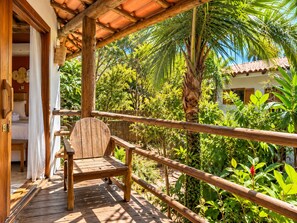A wooden deck with a bench, surrounded by lush greenery and a palm tree.