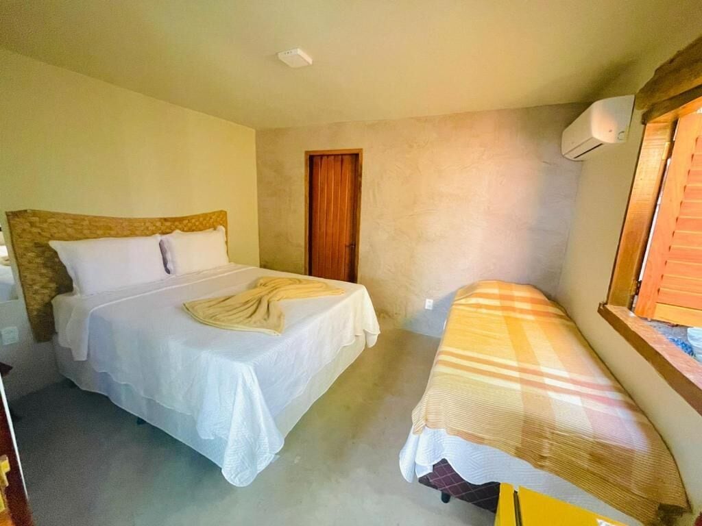 A bedroom with two beds, one with a wooden headboard and the other with a striped bedspread. There is a wooden door and a window with blinds.