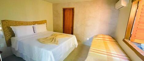 A bedroom with two beds, one with a wooden headboard and the other with a striped bedspread. There is a wooden door and a window with blinds.