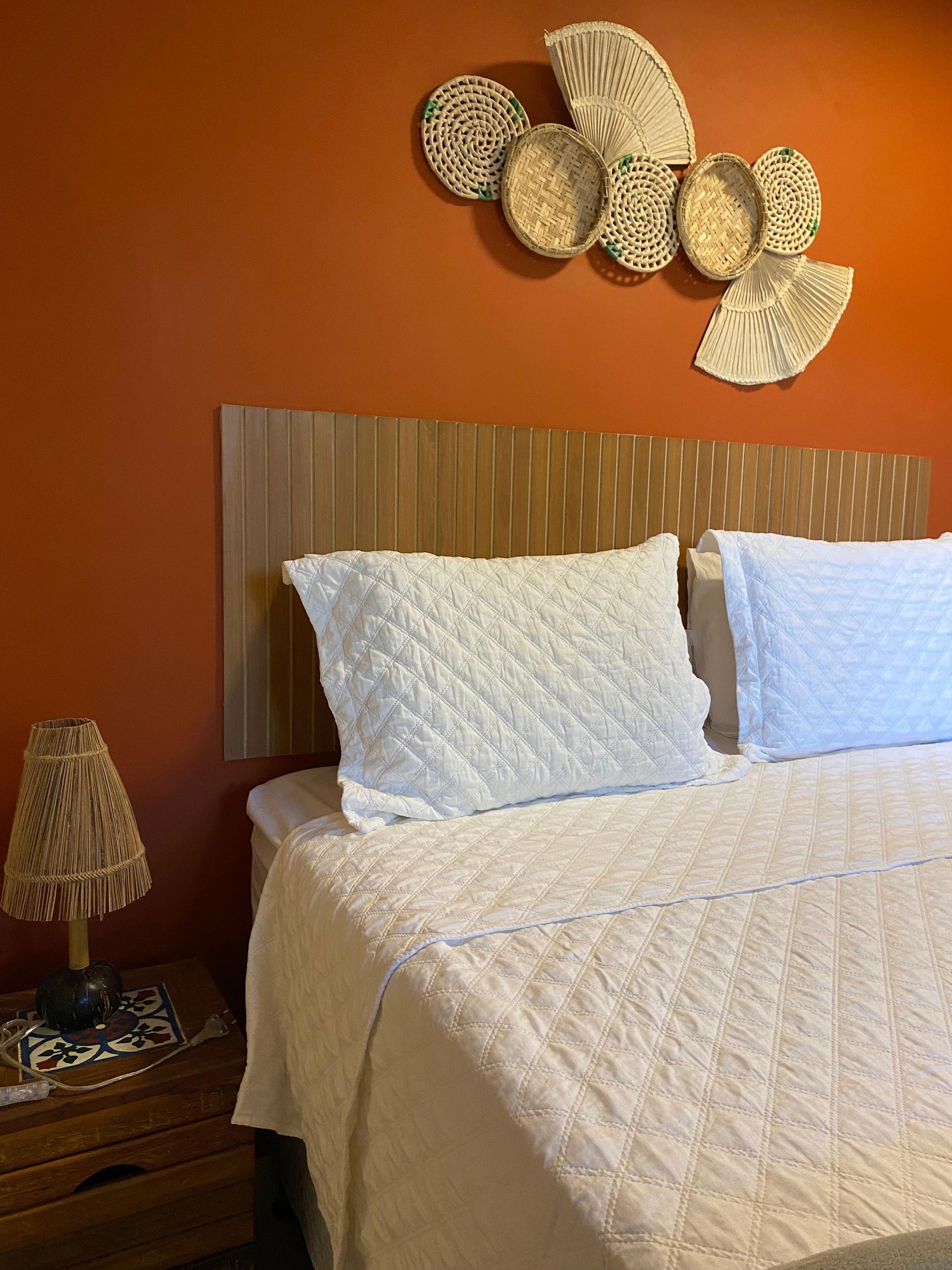 A bed with a quilted white duvet, a wooden headboard, and a wall-mounted decorative item.
