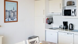 A small, clean kitchen with white cabinets, a microwave, and a coffee maker. There is a dining table with chairs and a framed picture on the wall. - Flat with a balcony overlooking the sea, 50 metres from the beach (Plougonvelin)