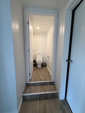 Un pasillo estrecho que conduce a un baño con un inodoro, un cubo de basura y una cesta.