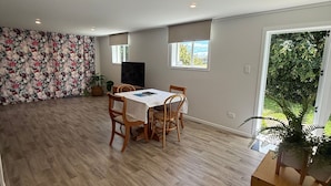 A spacious room with a wooden floor, a dining table with chairs, a large window, and a potted plant. - Cozy 2-bedroom House Rental in Whangārei, New Zealand (Whangarei)