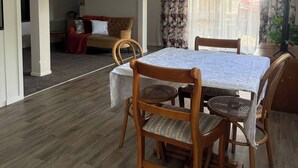 A dining area with a table and chairs, a sofa, and a window with curtains. - Cozy 2-bedroom House Rental in Whangārei, New Zealand (Whangarei)