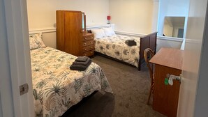A bedroom with two beds, a wooden dresser, a desk, and a chair. - Cozy 2-bedroom House Rental in Whangārei, New Zealand (Whangarei)