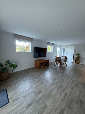 Amplia sala de estar con televisor de pantalla plana, piso de madera, mesa de comedor con sillas y una planta en maceta.