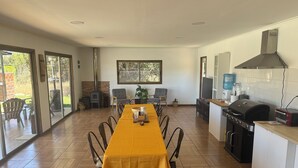 Un comedor con una mesa larga, sillas, una cocina con una parrilla y un amplio ventanal.