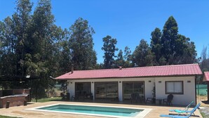 Una casa con piscina, sillas de patio y un área exterior techada.