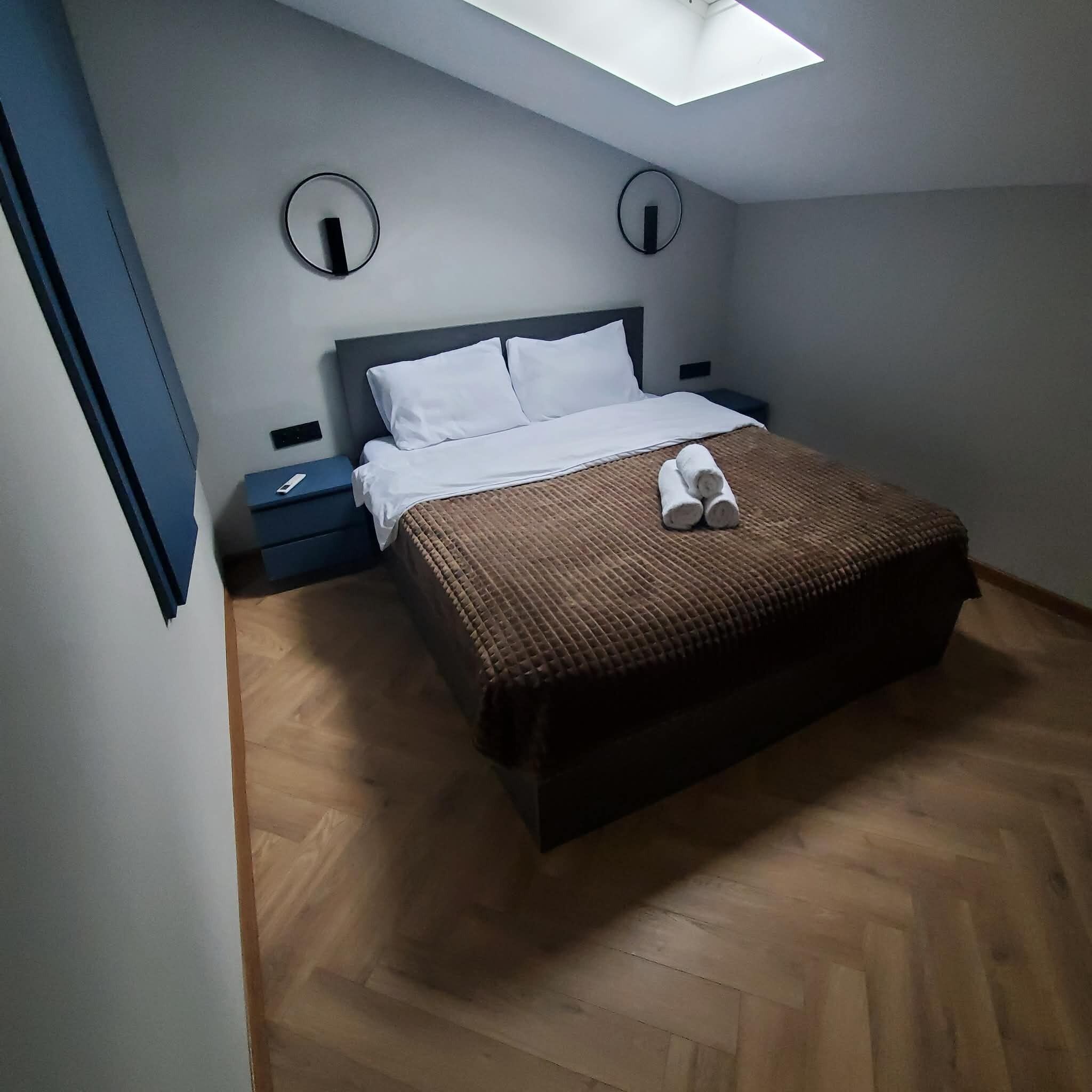 A bedroom with a bed, a nightstand, a wall clock, and a skylight.