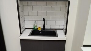Une cuisine de taille réduite, dotée d’un plan de travail noir, d’un crédence carrelée blanche et d’un évier noir.