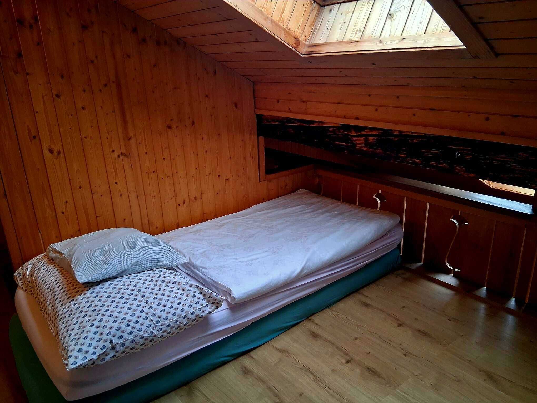 A small, single-bed room with wooden walls and a sloped ceiling.