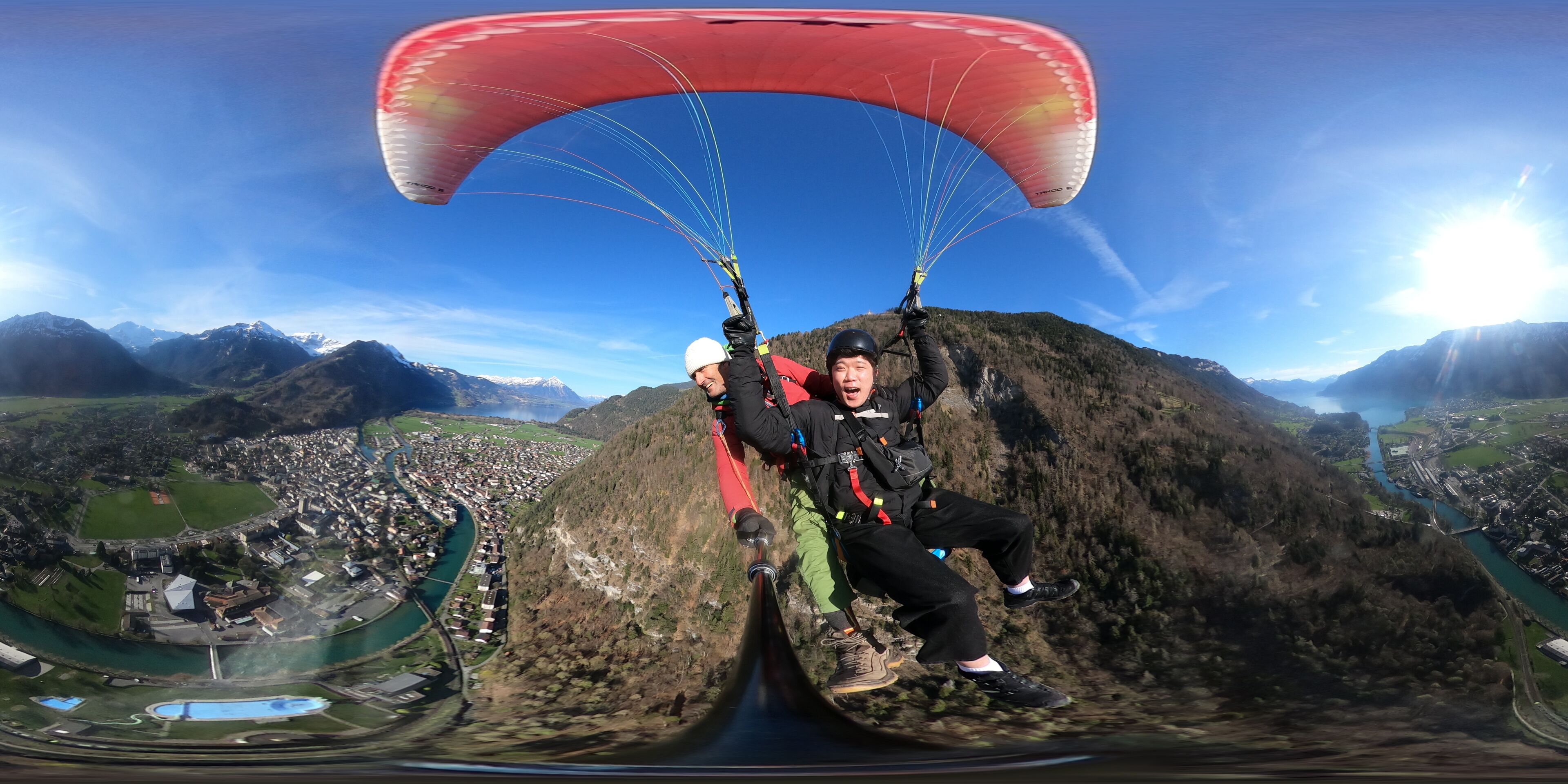 A person paragliding with a red canopy over a mountainous landscape.