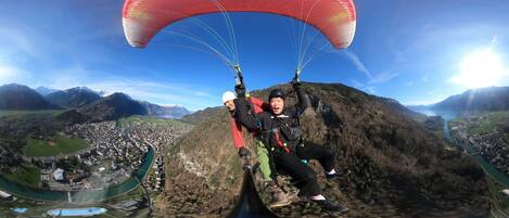 A person paragliding with a red canopy over a mountainous landscape.