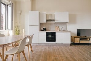 A modern kitchen with white cabinets, a built-in oven, and a television on a wooden stand. - Hostmate - Milano - Doria- Stazione Centrale (Milano)