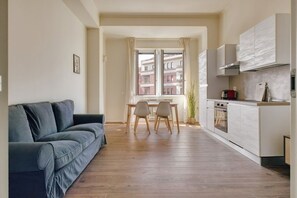 A modern living space with a sofa, dining table, chairs, and a kitchen area. - Hostmate - Milano - Doria- Stazione Centrale (Milano)