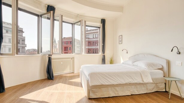 Ein Schlafzimmer mit großem Fenster, einem Bett, einem Heizkörper und einem kleinen Tisch.