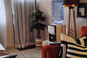 Ein Wohnzimmer mit einem großen Wasserspender, einer Topfpflanze und einem gestreiften Sofa.