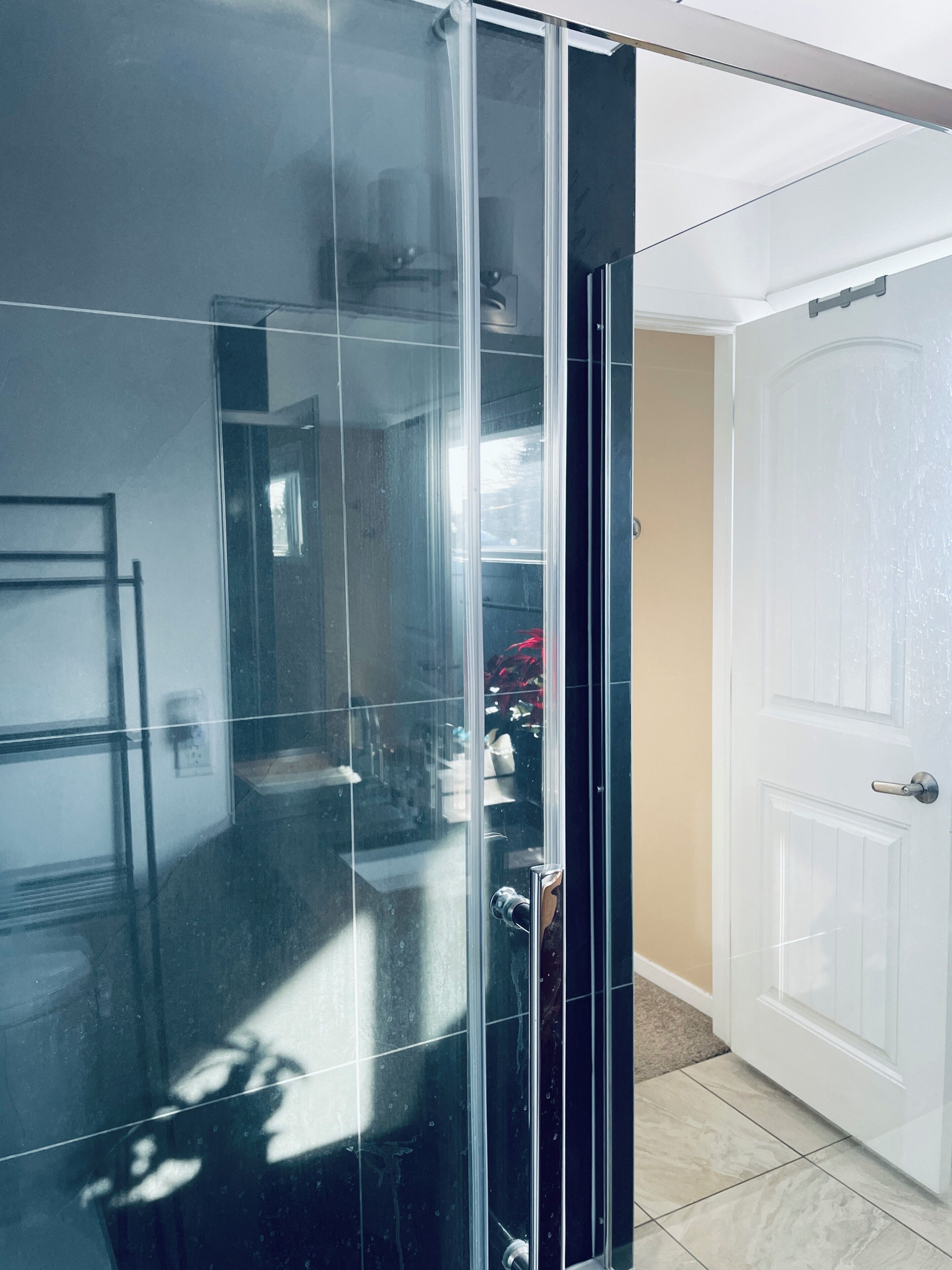 A modern bathroom with a glass shower enclosure, a white door, and a tiled floor.