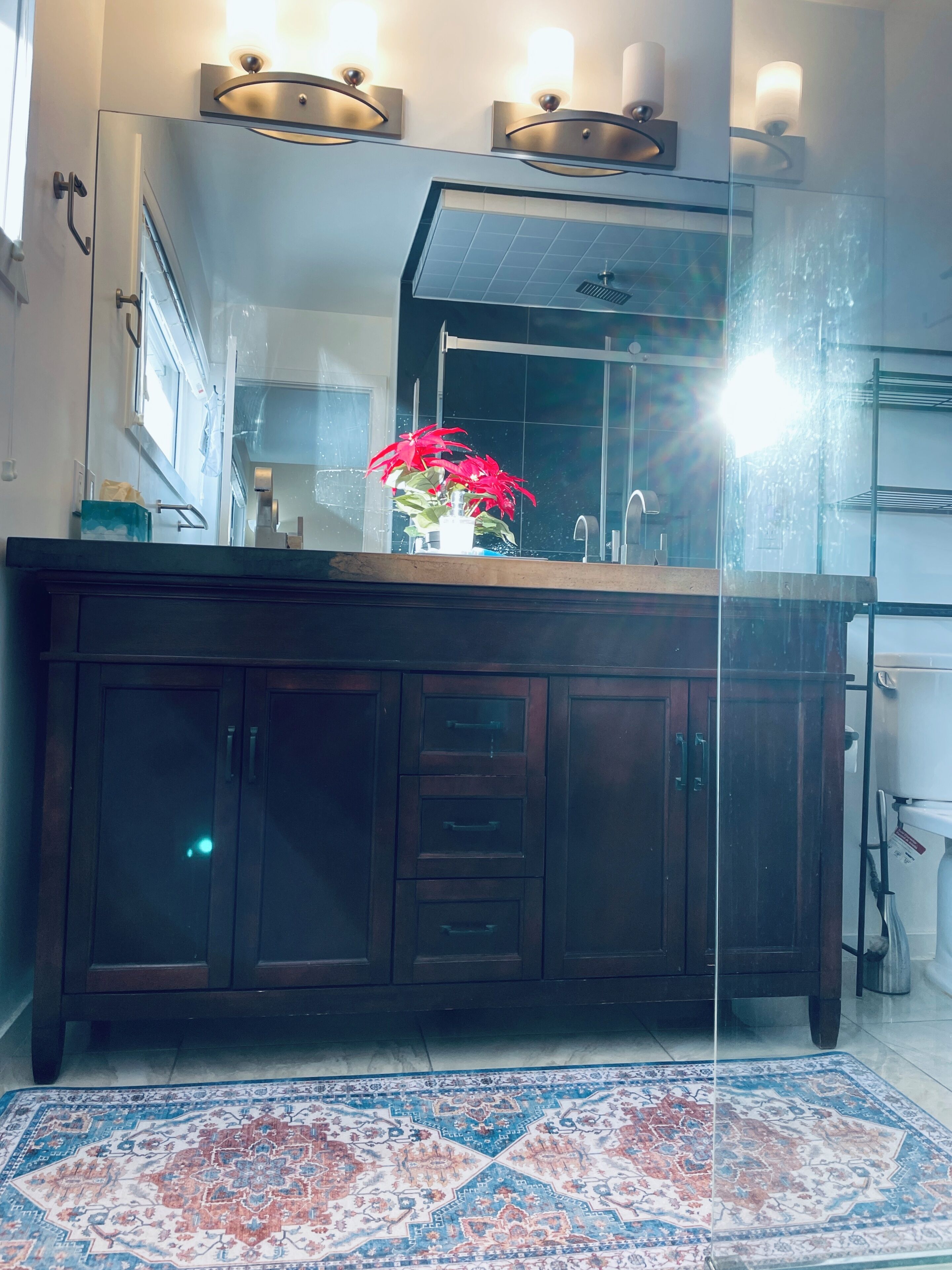 A modern bathroom with a dark wooden vanity, a glass shower enclosure, and a patterned rug on the floor.