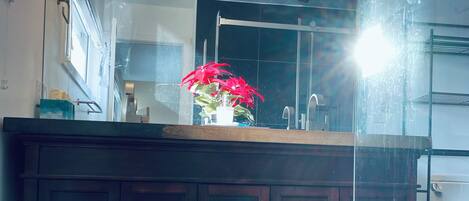 A modern bathroom with a dark wooden vanity, a glass shower enclosure, and a patterned rug on the floor.