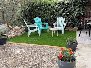 A patio area with two turquoise Adirondack chairs, a small white table, and a potted plant with orange flowers. - La Soleillade (Manosque)