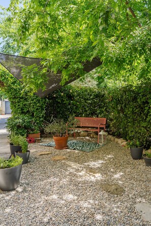 Un jardin avec un banc, des plantes en pot et un chemin de gravier.