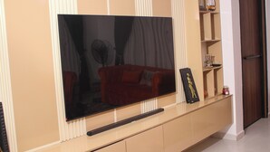A living room with a large flat-screen TV mounted on a wall, a red sofa, and a small shelf with decorative items. - Spacious 4-bedroom house in beautiful Lekki with AC and gym (Lekki)