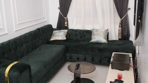 A modern living room with a dark green sectional sofa, two decorative pillows, a small round table, and a flat-screen TV mounted on the wall. - Spacious 4-bedroom house in beautiful Lekki with AC and gym (Lekki)