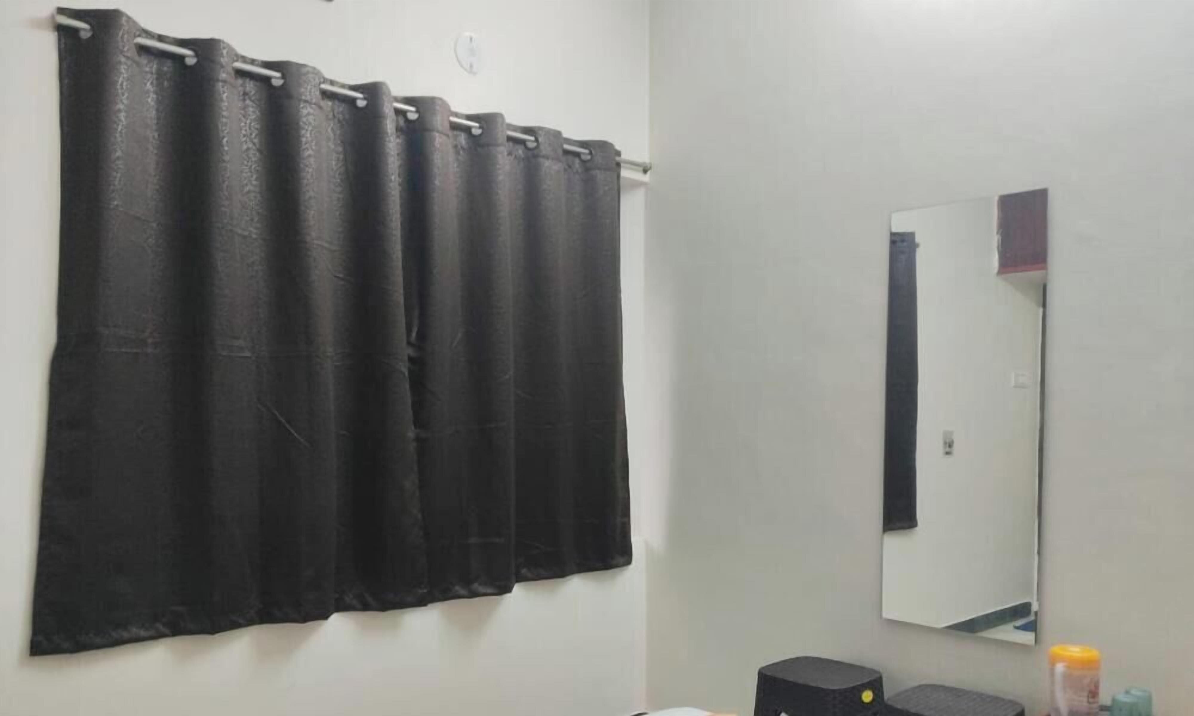 A bathroom with a black shower curtain, a mirror, and a small shelf with toiletries.