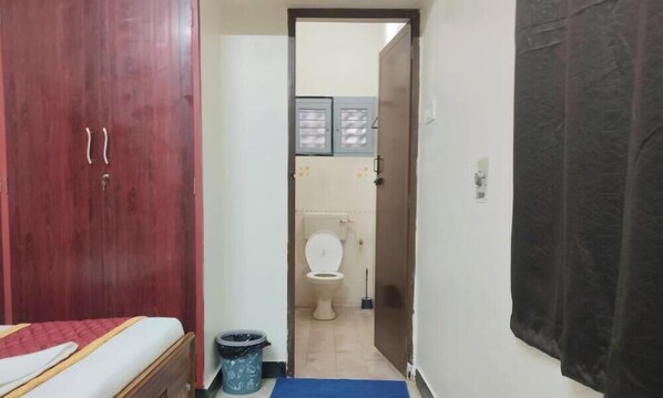 A bedroom with a bed, a wooden wardrobe, a blue mat, and a trash bin. - Grand Sarvik (Tiruchirappalli)