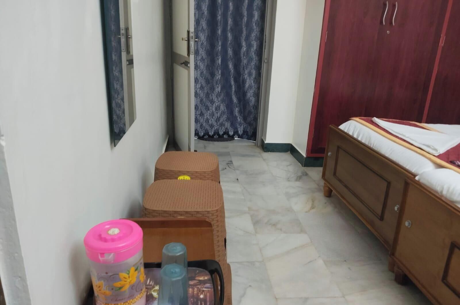 Un pasillo estrecho con una cama a la derecha, un armario y una pequeña mesa con un recipiente rosa y dos botellas azules.