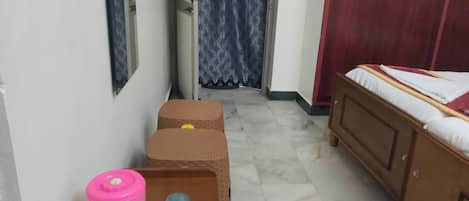 Un pasillo estrecho con una cama a la derecha, un armario y una pequeña mesa con un recipiente rosa y dos botellas azules.