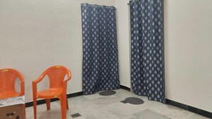 Ein Zimmer mit zwei orangefarbenen Plastikstühlen, einem blauen, gemusterten Vorhang und einem gefliesten Boden.